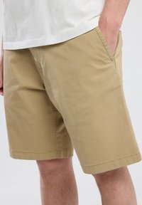 Beige shorts made of cotton with a smooth texture, featuring side pockets and a straight cut; no visible patterns or hardware accents.