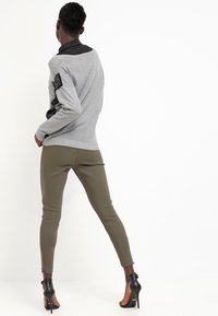 Un pull gris avec des détails noirs, associé à un pantalon ajusté vert olive et des chaussures à talons noirs, vu de dos.
