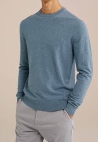 Ljusblå, crew-neck tröja i mjukt stickat material, med ribbade ärmslut och nederkant. Bärs över ljusgrå byxor med avslappnad passform.