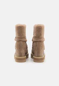 Botines de ante marrón con ribete de pelo sintético, adornados con rhinestones en los laterales y una suela de goma plana para mayor comodidad.