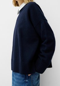 Pull en laine bleu marine avec ourlet et poignets côtelés. Conçu avec une coupe décontractée et des épaules tombantes. Associé à un jean en denim bleu clair.