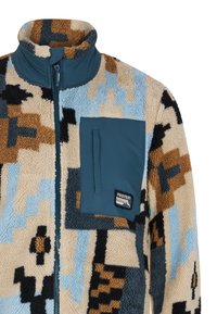 Fleece jakna s višebojnim geometrijskim uzorkom u bež, smeđoj, plavoj i crnoj boji, s zatvaranjem na patentni zatvarač i prsnom džepom u tirkiznoj boji.