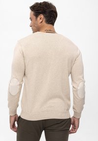 Beżowy sweter dziany z ribbowanymi mankietami i dołem. Posiada łaty na łokciach w dopasowanym odcieniu. Minimalistyczny design z okrągłym dekoltem.