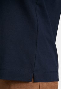 Marineblaue Baumwoll-T-Shirt mit seitlichem Schlitz und gesticktem Saum. Weicher Stoff und schlichtes Design. Fokussiert auf Einfachheit und Komfort in der Passform.