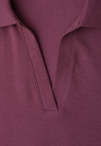 Gros plan sur un col de chemise tricotée violet avec une ouverture en V et des coutures visibles le long des bords.
