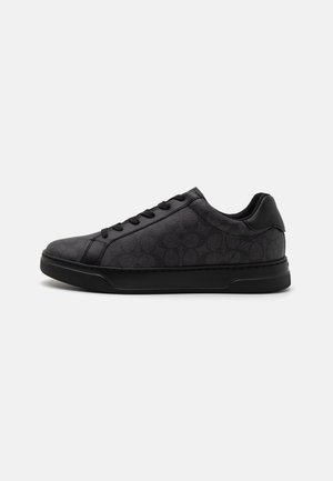 Zapatillas negras que presentan un material de cuero texturizado, patrón de logo tonal, puntera redonda, parte de arriba con cordones y suela de goma con un sutil diseño de tracción.