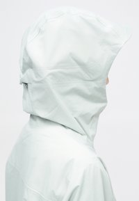Casaco à prova d'água cinza-claro com uma gola alta e capuz ajustável. Textura suave, design minimalista e detalhes de costura subtis.