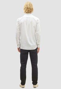 Weißes Langarmhemd aus Baumwolle mit lockerer Passform und Rückenfalte, kombiniert mit dunklen Hosen und hellen Schuhen.