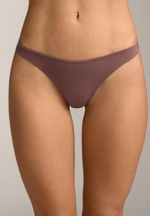 Donna che indossa biancheria intima stile bikini di colore malva, vista dalla vita alla parte superiore delle cosce su uno sfondo semplice.