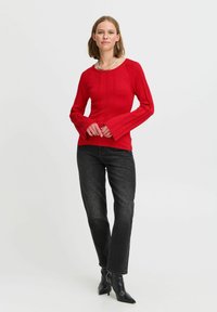 Röd ribbad långärmad topp med rund halsringning, i kombination med svarta högmidjade jeans och spetsiga svarta ankelstövlar.