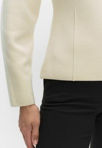 Crèmewitte gebreide top met een gestructureerd ontwerp, lange mouwen, naaddetails en een rechte zoom, gecombineerd met zwarte aansluitende broek.