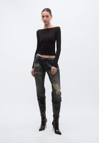 Bluză neagră cu mâneci lungi, combinată cu blugi albaștri destrămați, cu accente de ținte. Modelul poartă cizme înalte negre. Fundal simplu.