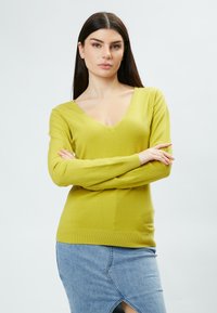 Maglione giallo a V con maniche lunghe, realizzato in materiale morbido. Presenta polsini e orlo a coste, abbinato a una gonna di jeans.