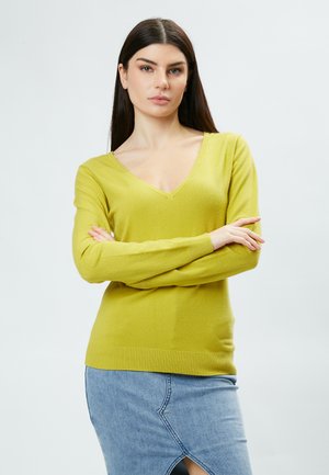 Maglione giallo a V con maniche lunghe, realizzato in materiale morbido. Presenta polsini e orlo a coste, abbinato a una gonna di jeans.