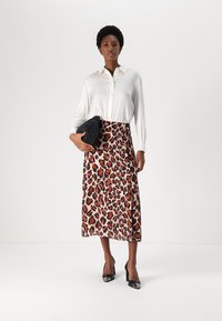 Camicia bianca a maniche lunghe abbinata a una gonna giusta a metà lunghezza con un motivo a stampa leopardata marrone e nera, accessoriosa con una clutch nera.