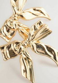 Goldene Haarklammern in Form von Schleifen, mit einer glänzenden Oberfläche, strukturierten Details und sanften Kurven.