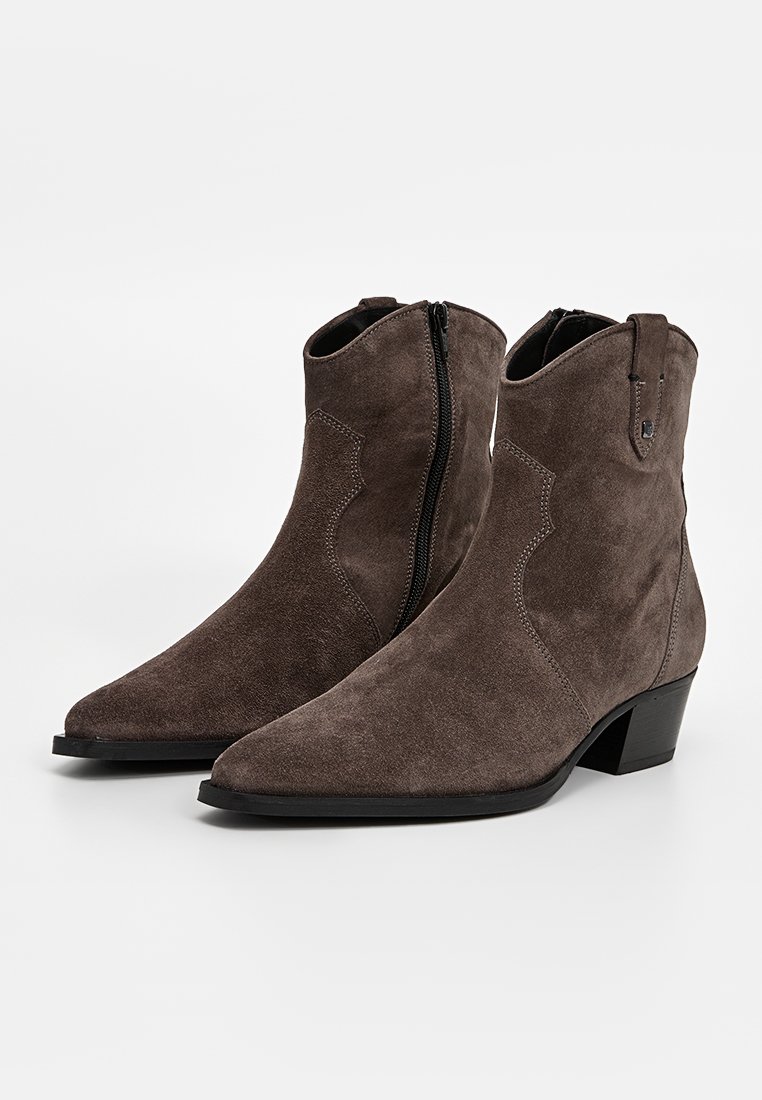 Stivali ankle in suede marrone con punta affusolata, zip laterale, cuciture decorative e tacco basso a blocco. Texture liscia e design minimalista.