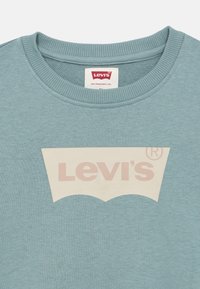 Φωτεινό γαλάζιο φούτερ με λογότυπο Levi's σε κρεμ απόχρωση σε χαρακτηριστικό κυρτό σχήμα. Λαιμόκοψη με ριμπ ύφανση προσθέτει υφή.