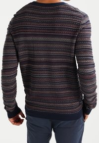 Stickad tröja i marinblått med ett strukturerat mönster där raderna växlar mellan vinröd, grå och krämfärgad. Ribbad mudd och fåll rundar av designen.