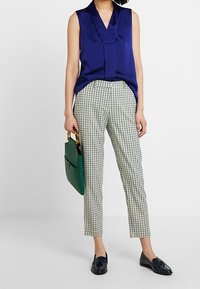 Námořnická bezrukávová blůza, bílo-zelené kostkované kalhoty, černé mokasíny a zelená kabelka s žlutou rukojetí. Hladká tkanina a přizpůsobený střih.