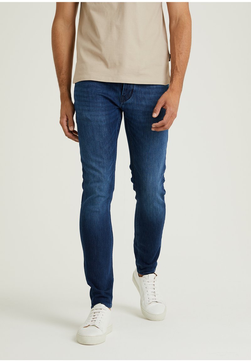 Donkerblauwe spijkerbroeken met een slim fit, met subtiele slijtage-looks, vijf-pocket ontwerp, gedragen met witte sneakers.