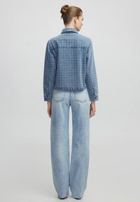 Giacca di jeans con ricamo, colore azzurro chiaro, polsini con bottoni e design cropped. Abbinata a jeans larghi di colore azzurro chiaro a vita alta.