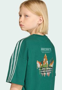 Zelené bavlnené tričko s krátkymi rukávmi, tromi bielymi pruhmi na každom pleci a logom Minecraft s pixelovou grafikou na chrbte.