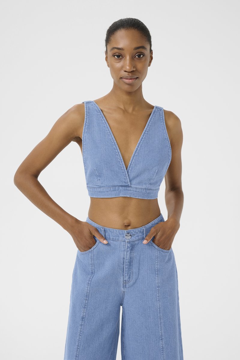 Svetlomodrý deninový crop top s hlbokým V-výstrihom a širokými ramienkami. Dizajn sa vyznačuje štruktúrovanou siluetou a je kombinovaný s vysokými nohavicami v rovnakom odtieni.