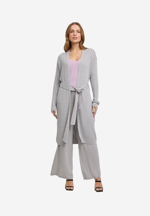 Un cardigan en tricot gris à manches longues avec une ceinture à nouer, par-dessus un haut violet clair avec un motif côtelé, associé à un pantalon gris à jambes larges.