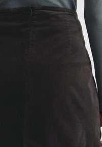 Zwarte corduroy rok met een gladde textuur, hoge taille, rits aan de zijkant en subtiele verticale lijnen, gedeeltelijk zichtbaar met een blauwe trui.