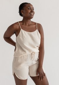 Beige getextureerde mouwloze top met verstelbare bandjes, gecombineerd met bijpassende shorts met zijsplitten en een trekkoord in de taille.