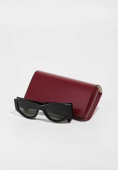 Must-have mustikkamusta kissasilmäsunglassit tummilla linsseillä, jotka on pakattu burgundinväriseen nahkakoteloon, jossa on painettu "GUCCI". Luonnollinen, moderni muotoilu.