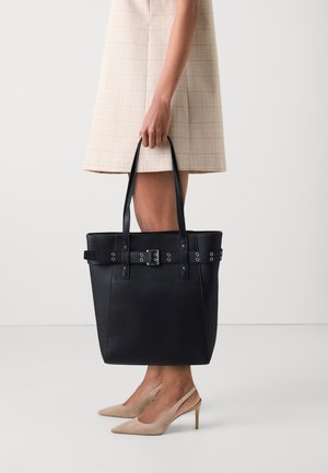 Sac fourre-tout en cuir noir au format structuré, avec des accents en métal argenté et des poignées doubles. Il dispose d'une sangle similaire à une ceinture avec des œillets.
