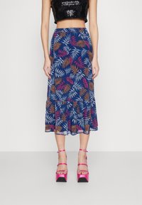 Spódnica midi w kwiatowy wzór w kolorze granatowym, z liściastymi motywami w odcieniach różu, pomarańczy i bieli, z rozkloszowanym dołem i przejrzystością. Noszona z różowymi, platformowymi szpilkami.