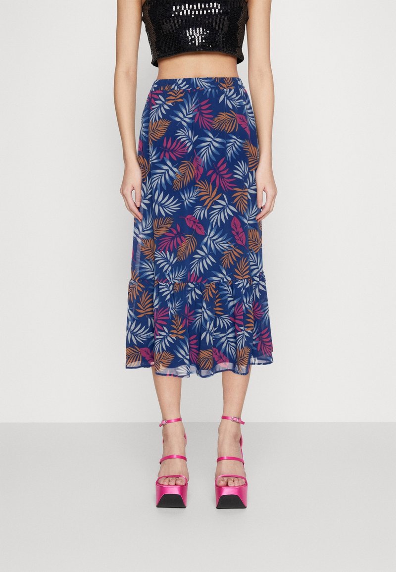 Spódnica midi w kwiatowy wzór w kolorze granatowym, z liściastymi motywami w odcieniach różu, pomarańczy i bieli, z rozkloszowanym dołem i przejrzystością. Noszona z różowymi, platformowymi szpilkami.