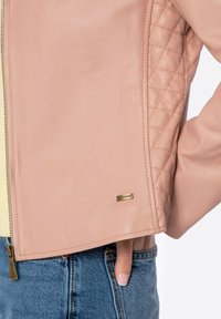 Giacca di pelle rosa chiaro con texture a trapunta sulle maniche, dettagli con zip dorati e un piccolo tag in metallo del marchio vicino all'orlo.