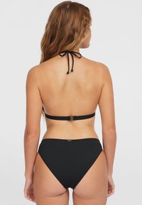 Czarny zestaw bikini z halterem i zapięciem na wiązanie. Góra ma minimalne zasłonięcie, a wysoki stan spodenek zapewnia pełne przykrycie.