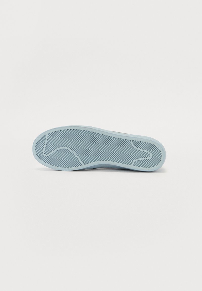Semelle de sneaker bleu clair présentant un motif en chevron pour une meilleure adhérence, avec une surface texturée lisse.