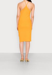 Sukienka bodycon w jaskrawym pomarańczowym kolorze, wykonana z elastycznego materiału. Posiada halter neck z krzyżującymi się ramiączkami, długość do kolan oraz minimalistyczny styl.