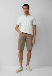 Weißes Polo mit V-Ausschnitt und kurzen Ärmeln, kombiniert mit beigefarbenen Shorts und weißen Sneakers mit beigen Akzenten. Einfaches und legeres Outfit.