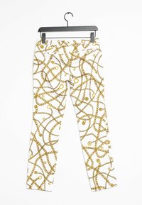 Pantalones blancos con un patrón de cadenas doradas y acentos circulares, con un corte ajustado y una cinturilla estándar, colgados en una percha negra.