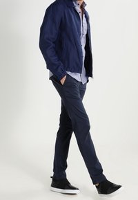 Marine bomberjack over een geruit shirt, gecombineerd met marineblauwe broek en zwarte instappers. De outfit heeft een casual, ontspannen pasvorm.