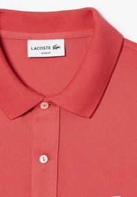 Camisa polo roja con un tejido texturizado, diseño ajustado, cuello plano y una tapeta de un solo botón; presenta un logo en el pecho.