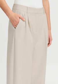 Beige wijde broek van gladde stof, met zijzakken en een geplooid ontwerp aan de voorkant. Focus op strakke lijnen en een tailor-made uitstraling.