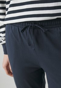 Granatowe dresy z elastycznym pasem i sznurkiem do regulacji. Na górze znajduje się warstwowy, paskowany top z długimi rękawami. Wykonane z miękkiego bawełnianego materiału, w luźnym kroju.