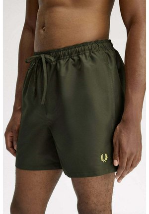 Uomo che indossa pantaloncini da bagno verde scuro con vita elastica, coulisse e piccolo logo giallo di alloro sulla gamba sinistra.