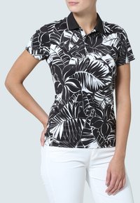 Černobílý polo tričko s odvážným tropickým vzorem listů, krátkými rukávy a černým límečkem. Nosené s bílými kalhotami.