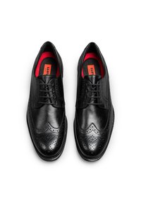 Scarpe da uomo in pelle nera con design a wingtip, perforazioni dettagliate, superficie liscia e plantari rossi vivaci. Chiusura con lacci e punta arrotondata.