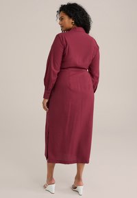 Rochie burgundă, cu nasturi, cu mâneci lungi, talie marcată cu o curea și fante laterale, realizată dintr-un material neted. Purtați cu sandale albe cu toc.