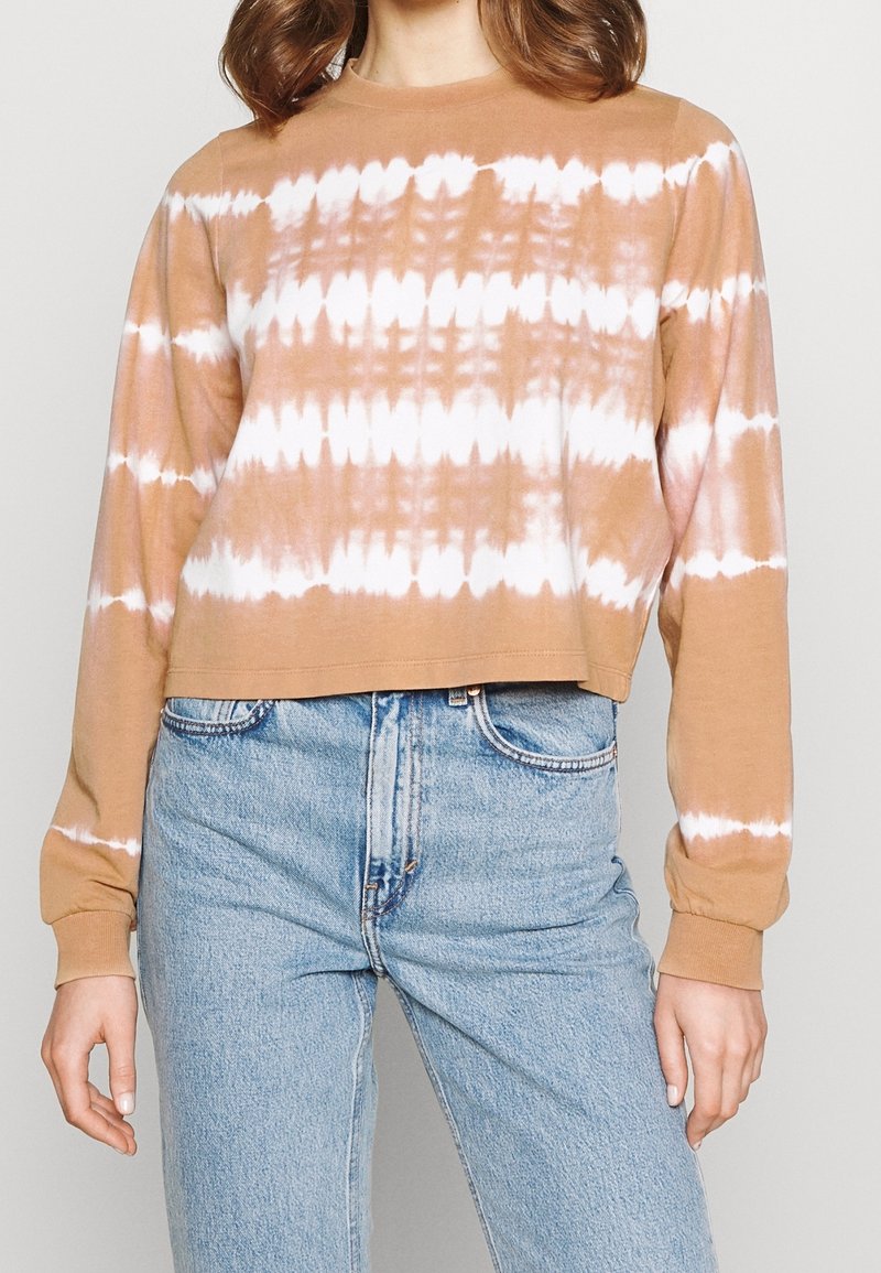 Hnědá cropovaná mikina s bílým batikovým vzorem, dlouhými rukávy, kulatým výstřihem a měkkou texturou, v kombinaci se světle modrými džínami.